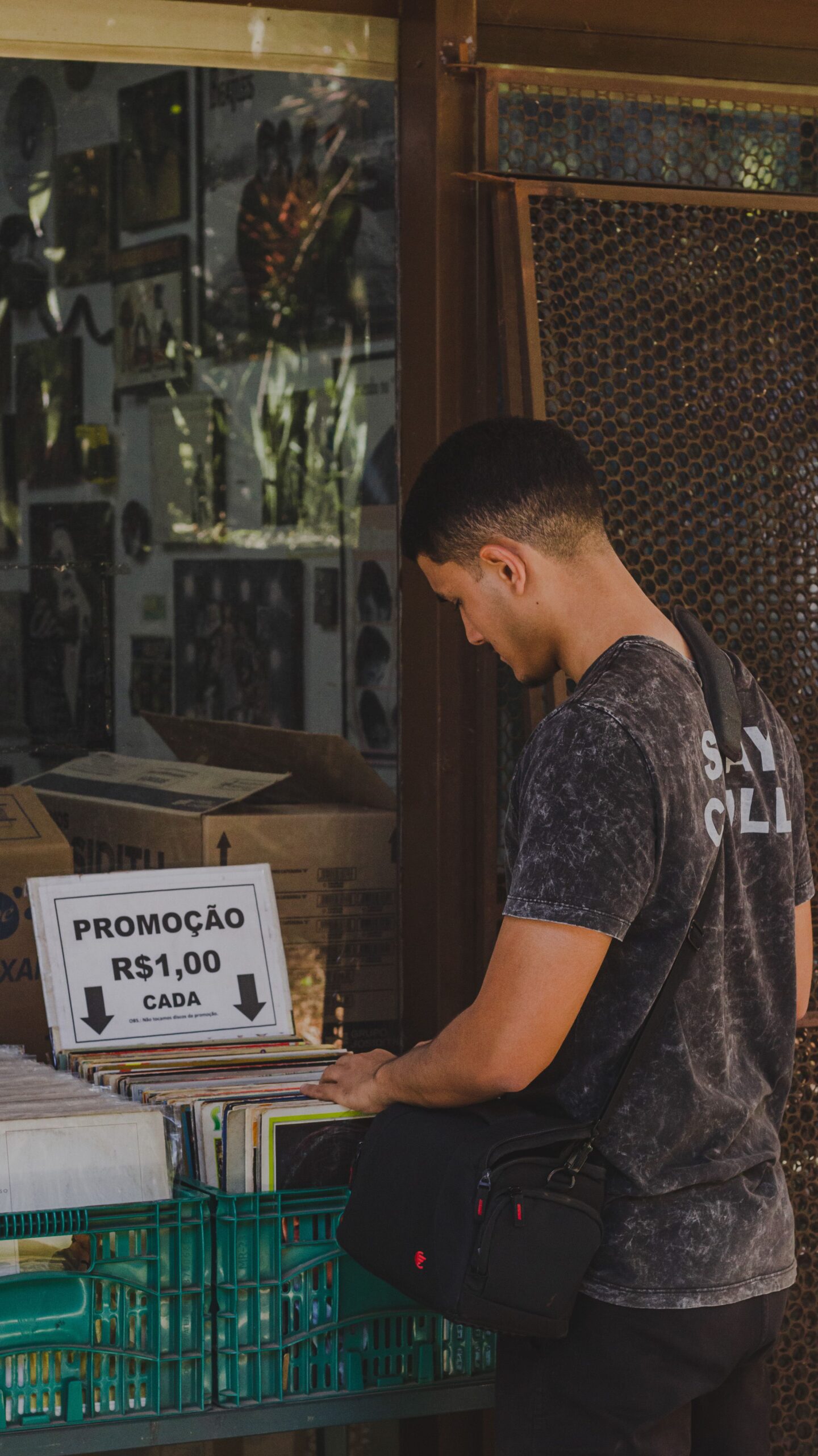 Man browsing items at a street market in Brasília, checking promotions. Urban and casual scene.